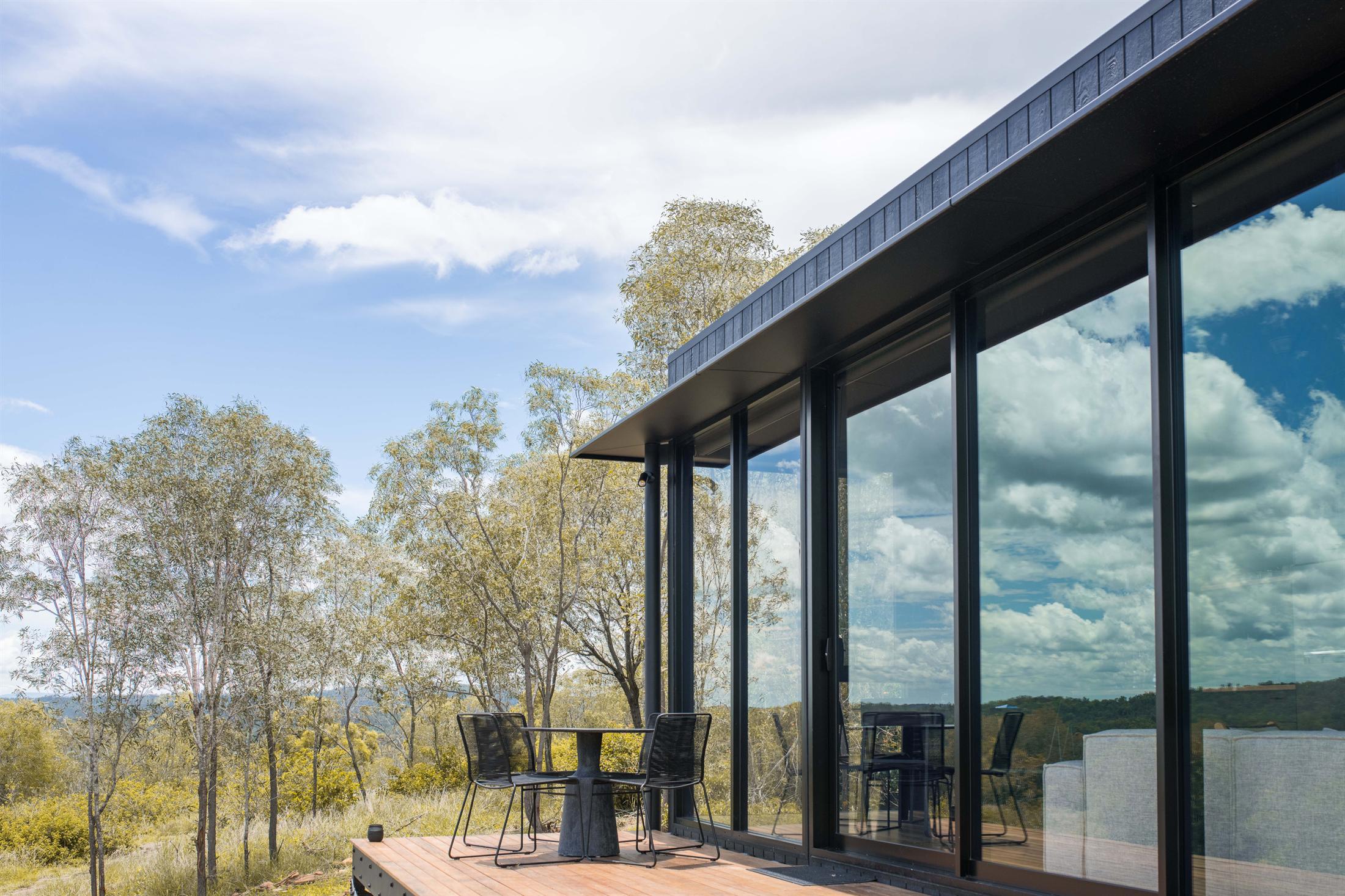 Black-framed sliding glass doors opening onto a timber deck in the bush