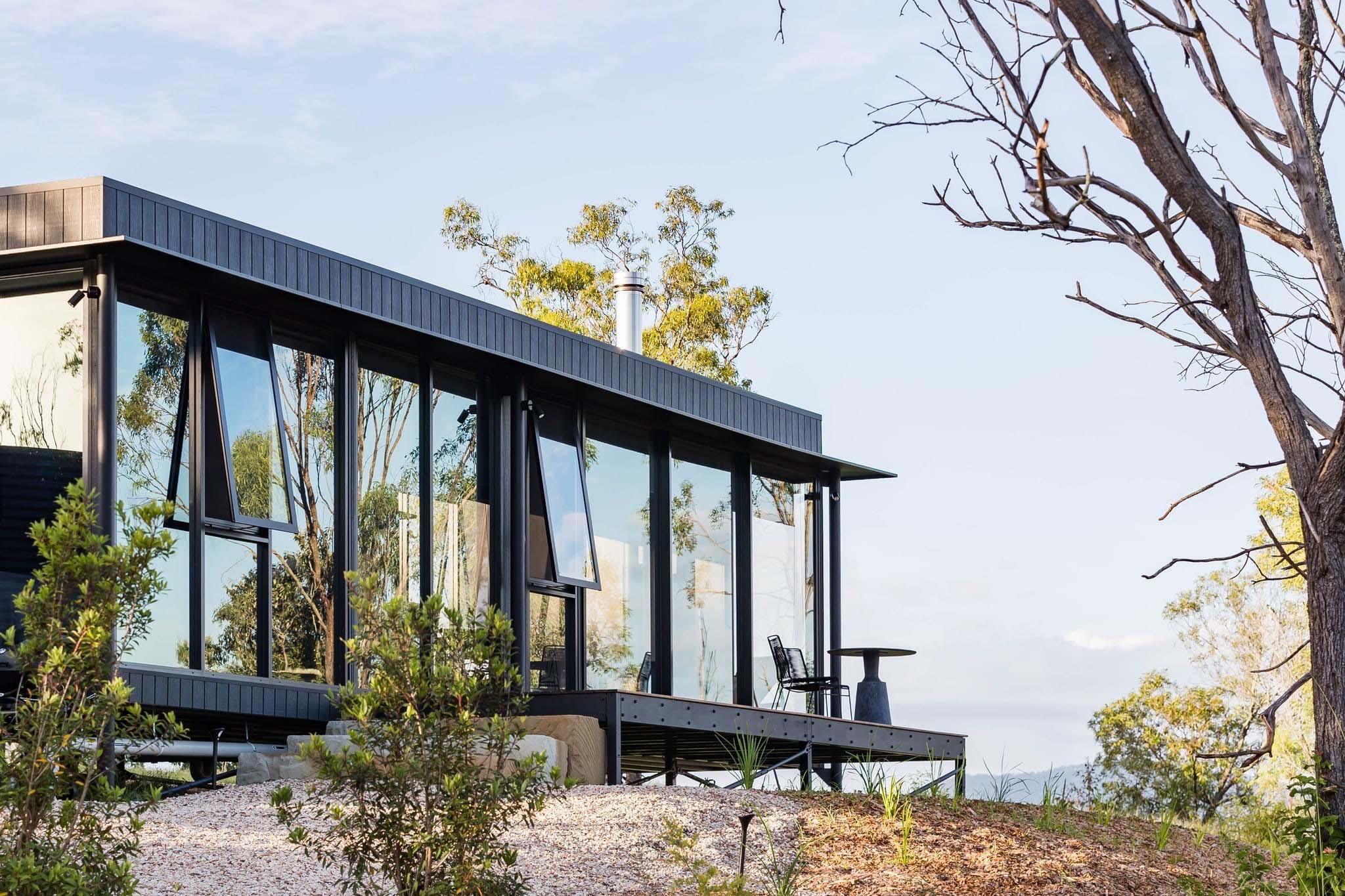 Pavilion with black-framed awning windows open to the bush