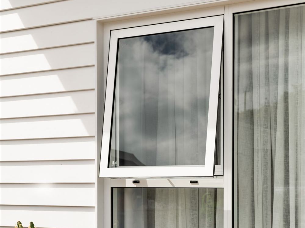 White awning window opened above a fixed pane on a white weatherboard home